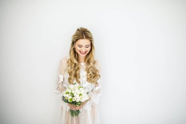 Beyaz bir odada buketi olan güzel sarışın bir gelinin portresi.