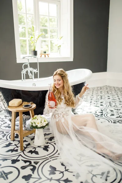 一个年轻美丽的金发新娘的肖像 浴室里有一瓶香槟 — 图库照片
