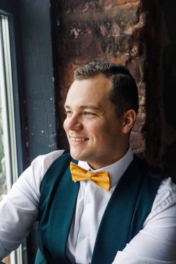 Çatı katındaki pencerenin yanında oturan klasik takım elbiseli genç adam.