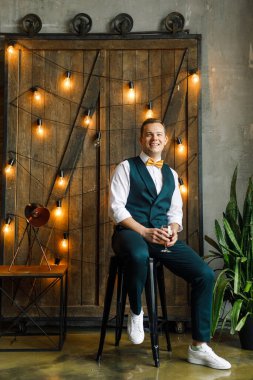 Klasik takım elbiseli genç adam ahşap kapılar ve ampullerin arkasındaki çatı katında oturur ve viski içer.