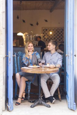 Mavi elbiseli çift, şehir manzaralı mavi kapıların yakınındaki bir restoranda yemek yiyorlar.