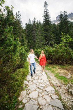 Genç bir çift, kırmızı elbiseli bir kız ve beyaz tişörtlü ve mavi pantolonlu bir adam Polsha 'daki Tatra Ulusal Parkı' nda yürüyorlar.