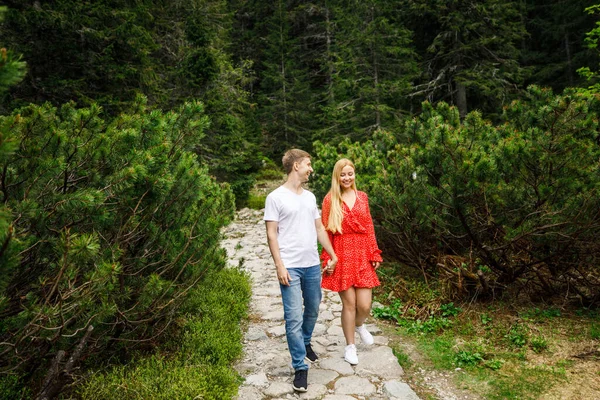 a young couple, a girl in a red dress, and a man in a white T-shirt and blue pants, are walking in the Tatra National Park in Polsha