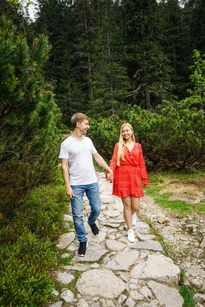 若いカップル赤いドレスの女の子白いTシャツと青いパンツの男がポルシャのタトラ国立公園を歩いています — ストック写真