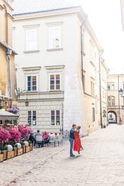 Genç bir çift şık giyiniyor, kırmızı elbiseli bir kız, mavi gömlekli ve mavi pantolonlu bir adam, Krakow Polonya sokaklarında yürüyor.