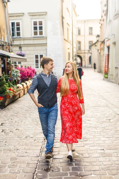 a young couple is stylishly dressed, a girl in a red dress, a man in a blue shirt and blue pants, walk the streets in Krakow Poland