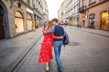 Genç bir çift şık giyiniyor, kırmızı elbiseli bir kız, mavi gömlekli ve mavi pantolonlu bir adam, Krakow Polonya sokaklarında yürüyor.