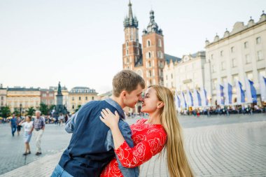 Genç bir çift şık giyiniyor, kırmızı elbiseli bir kız, mavi gömlekli ve mavi pantolonlu bir adam, Krakow Polonya sokaklarında yürüyor.