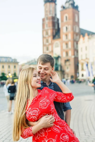 若いカップルはスタイリッシュに服を着て赤いドレスの女の子青いシャツと青いパンツの男はポーランドのクラクフの街を歩く — ストック写真
