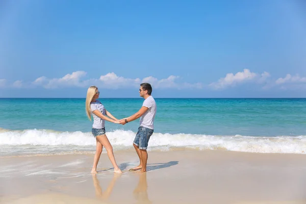 Giovane coppia felice sulla spiaggia sorridente tenendosi per mano intorno a vicenda. Storia d'amore — Foto Stock