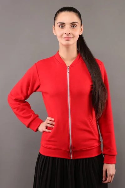 Young hipster girl wearing blank red cotton zip up sweatshirt with copy space for your design or logo, mock-up of ltemplate womens hoodie, grey wall in the background