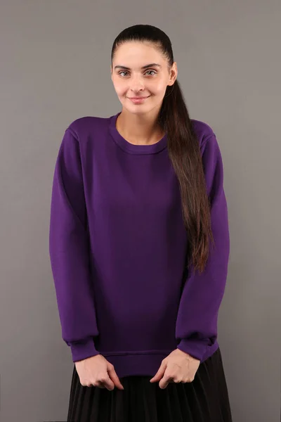 Young hipster girl wearing blank purple cotton sweatshirt with copy space for your design or logo, mock-up of purple template womens hoodie, grey wall in the background
