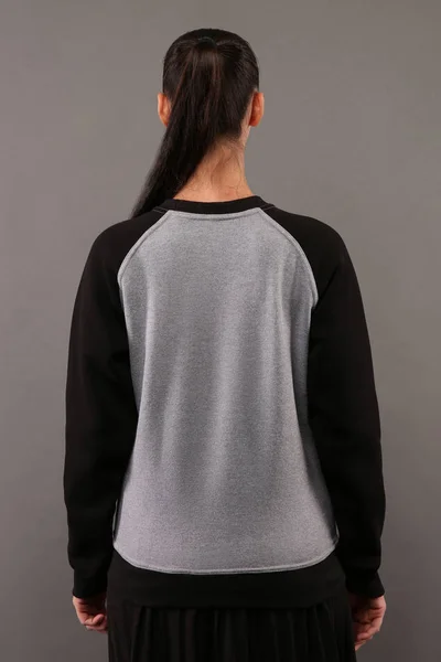 Tasarım veya logo, ltemplate Bayan kapşonlu mock-up için kopya alanı ile mürettebat boyun ve raglan kollu boş gri ve siyah pamuklu kazak giyen genç hippi kız arkasında
