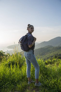 Hippi kız günbatımı sisli dağ tepe üzerinde zevk sırt çantası ile. Arka plan görünüm mockup üzerinde turist Gezgin.