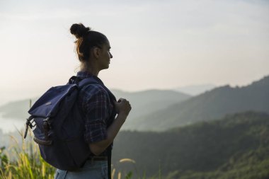 Hippi kız günbatımı sisli dağ tepe üzerinde zevk sırt çantası ile. Arka plan görünüm mockup üzerinde turist Gezgin.