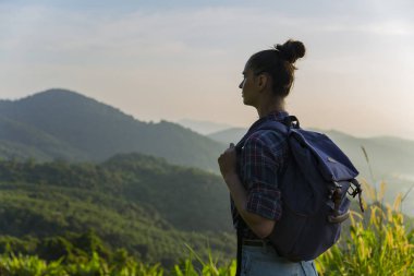 Hippi kız günbatımı sisli dağ tepe üzerinde zevk sırt çantası ile. Arka plan görünüm mockup üzerinde turist Gezgin.