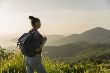 Hippi kız günbatımı sisli dağ tepe üzerinde zevk sırt çantası ile. Arka plan görünüm mockup üzerinde turist Gezgin.