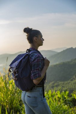 Hippi kız günbatımı sisli dağ tepe üzerinde zevk sırt çantası ile. Arka plan görünüm mockup üzerinde turist Gezgin.