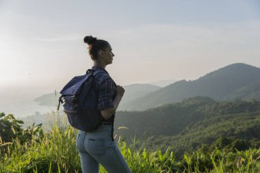 Hippi kız günbatımı sisli dağ tepe üzerinde zevk sırt çantası ile. Arka plan görünüm mockup üzerinde turist Gezgin.