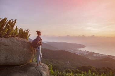 Hippi kız en yüksek dağında gün batımı zevk sırt çantası ile. Arka plan Vadisi manzara görünümü mockup üzerinde turist gezgin. Tonda, instagram vintage filtre.