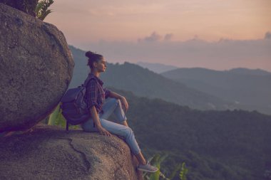 Hippi kız en yüksek dağında gün batımı zevk sırt çantası ile. Arka plan Vadisi manzara görünümü mockup üzerinde turist gezgin. Tonda, instagram vintage filtre.