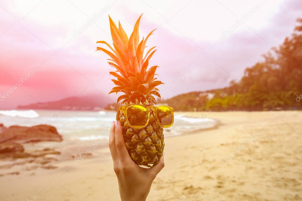 Pineapple fruit in sunglasses on hand against turquoise caribbean sea water. Tropical summer vacation concept. Toned