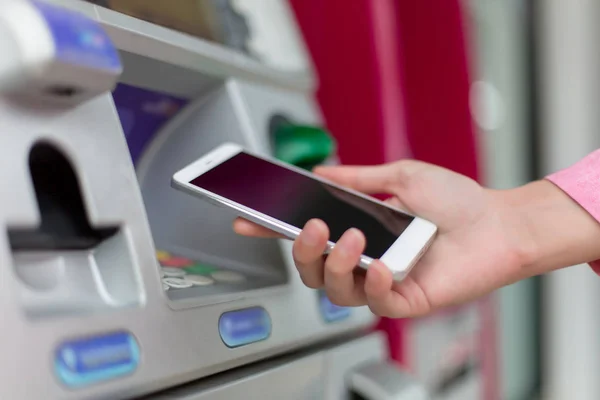 Woman holding a Smartphone financial transactions online on the background, ATM cabinet. Online NFC Banking Concept