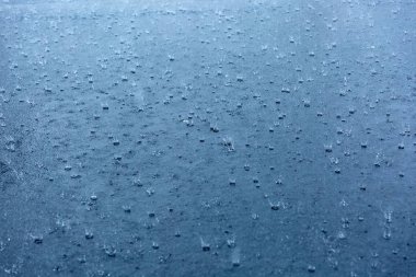 mavi gökyüzünün yansıması ile bir su birikintisi içinde dalgalanan yağmur damlaları