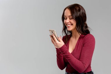 Modaya uygun küpeleri olan neşeli, duygusal genç Avrupalı bir kadın elinde akıllı bir telefon, kameraya neşeyle gülümserken arkadaşına ilginç bir makaleyi tekrar anlatıyor.