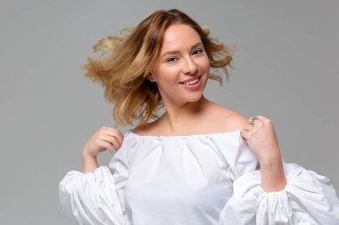 Tek renkli arka planda uzun saçlı, güzel gülümseyen ve poz veren sarışın kadının portresi.