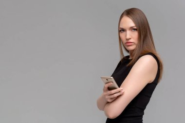 Uzun saçlı, modern cep telefonunu elinde tutan, sosyal ağlarda gezinen, neşeli bir ifadesi olan, günlük kıyafet giyen, tek renkli arka planda izole edilmiş, mesaj alan bir genç.