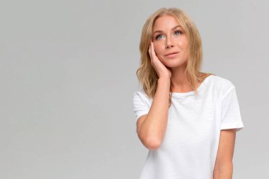 Heyecanlı, beyaz tişörtlü, arka plan stüdyo resminde yalnız poz veren genç, sarışın bir kız. İnsanların yaşam tarzı yeni bir fikir. Kopyalama alanı oluştur.