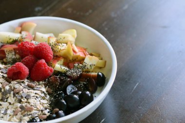 karışık meyve ve kahverengi ahşap masa üzerinde beyaz bir kase mısır gevreği