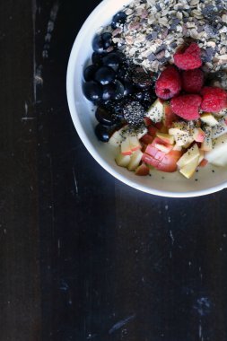 karışık meyve ve kahverengi ahşap masa üzerinde beyaz bir kase mısır gevreği