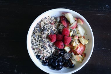 karışık meyve ve kahverengi ahşap masa üzerinde beyaz bir kase mısır gevreği