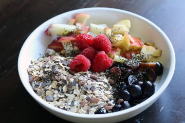 karışık meyve ve kahverengi ahşap masa üzerinde beyaz bir kase mısır gevreği