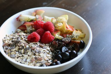 karışık meyve ve kahverengi ahşap masa üzerinde beyaz bir kase mısır gevreği