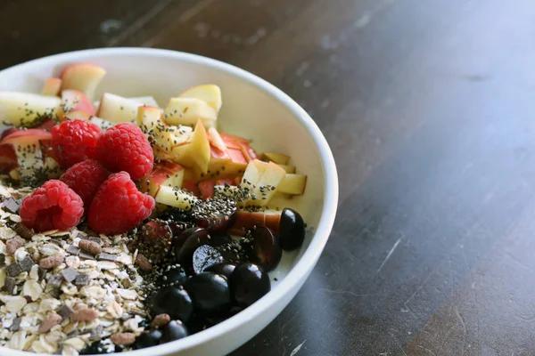 karışık meyve ve kahverengi ahşap masa üzerinde beyaz bir kase mısır gevreği