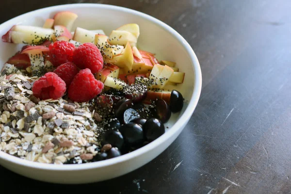 karışık meyve ve kahverengi ahşap masa üzerinde beyaz bir kase mısır gevreği