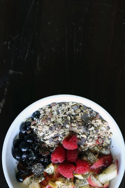 Frutas misturadas e cereais em uma tigela branca na mesa de madeira marrom — Fotografia de Stock