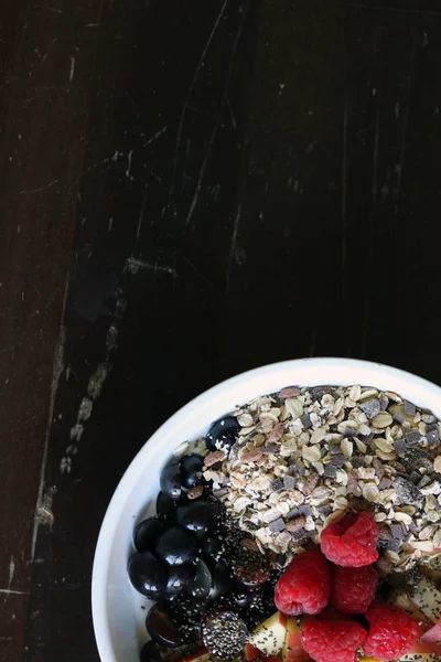 Gemischtes Obst und Müsli in einer weißen Schüssel auf einem braunen Holztisch — Stockfoto