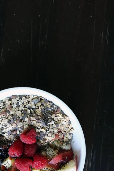 Gemischtes Obst und Müsli in einer weißen Schüssel auf einem braunen Holztisch — Stockfoto