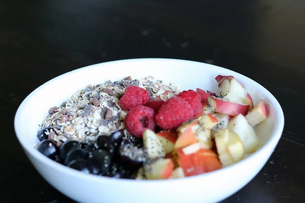 Gemischtes Obst und Müsli in einer weißen Schüssel auf einem braunen Holztisch — Stockfoto