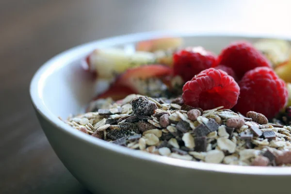 Gemischtes Obst und Müsli in einer weißen Schüssel auf einem braunen Holztisch — Stockfoto