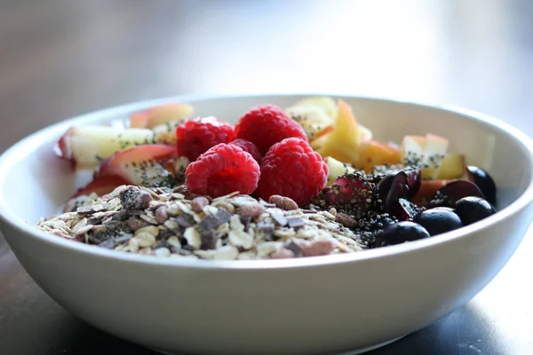 Gemischtes Obst und Müsli in einer weißen Schüssel auf einem braunen Holztisch — Stockfoto