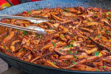 Arkaplanda büyük bir tavada ahtapot filetoları var.