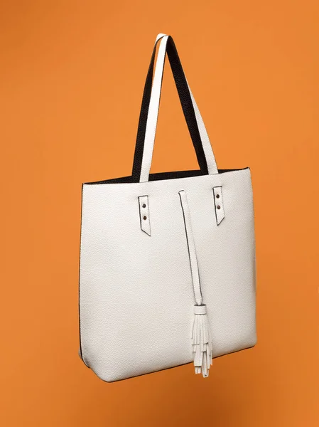 Beautiful luxury leather female white bag on an orange background