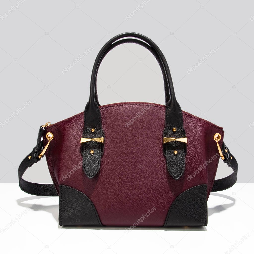 Luxurious beautiful burgundy with black accents leather bag on a gray background