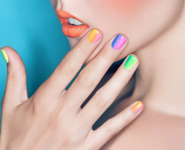 Beautiful female lips and hand with rainbow manicure on nails with makeup closeup
