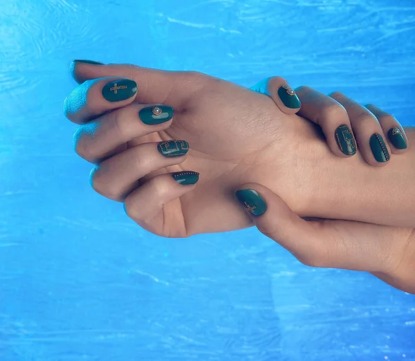 Hermosas manos femeninas con colorido verde brillante y manicura de oro en las uñas de cerca, fondo nevado — Foto de Stock